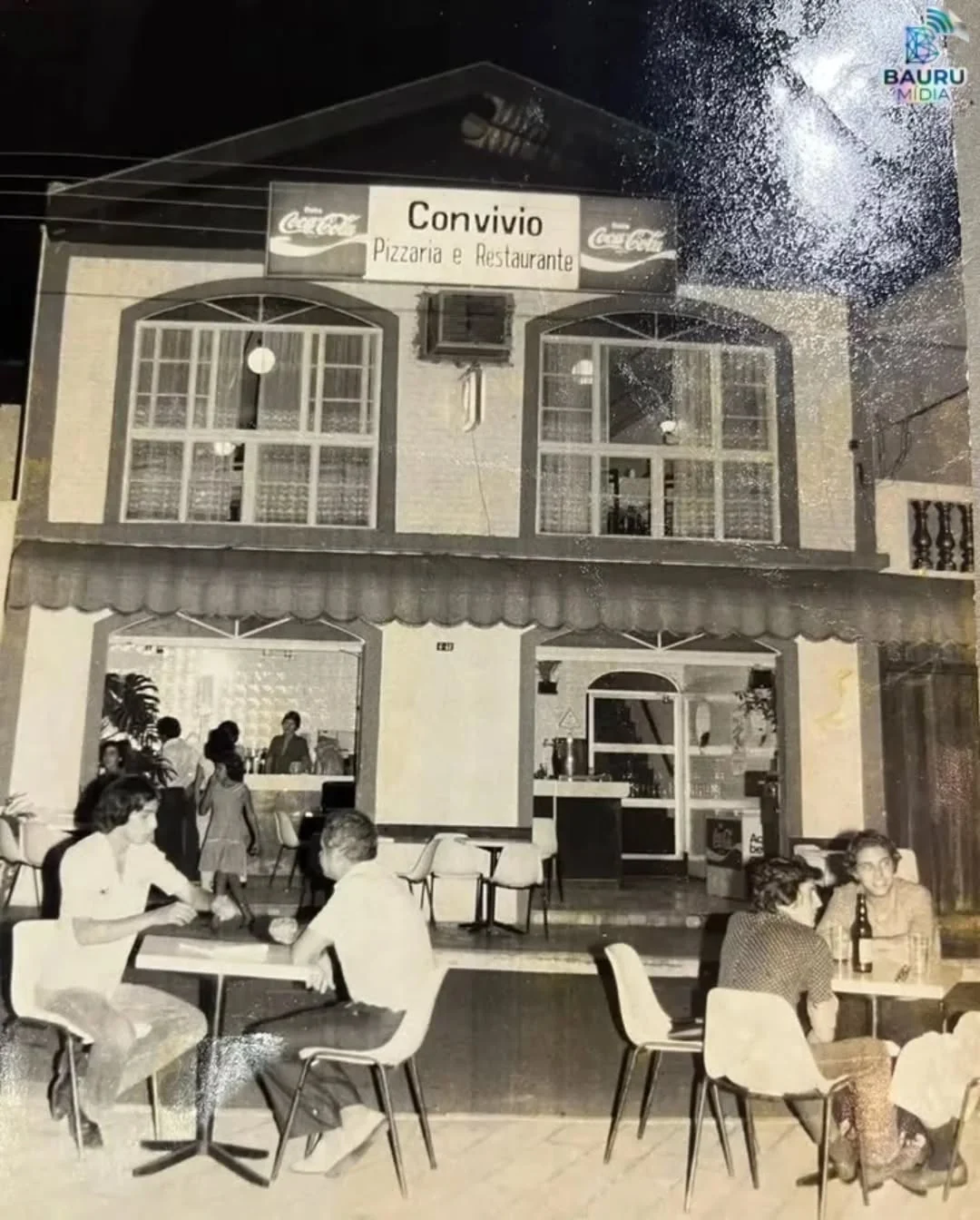 Fachada antiga do Convívio Pizzaria e Restaurante em foto preto e branco, com mesas na calçada