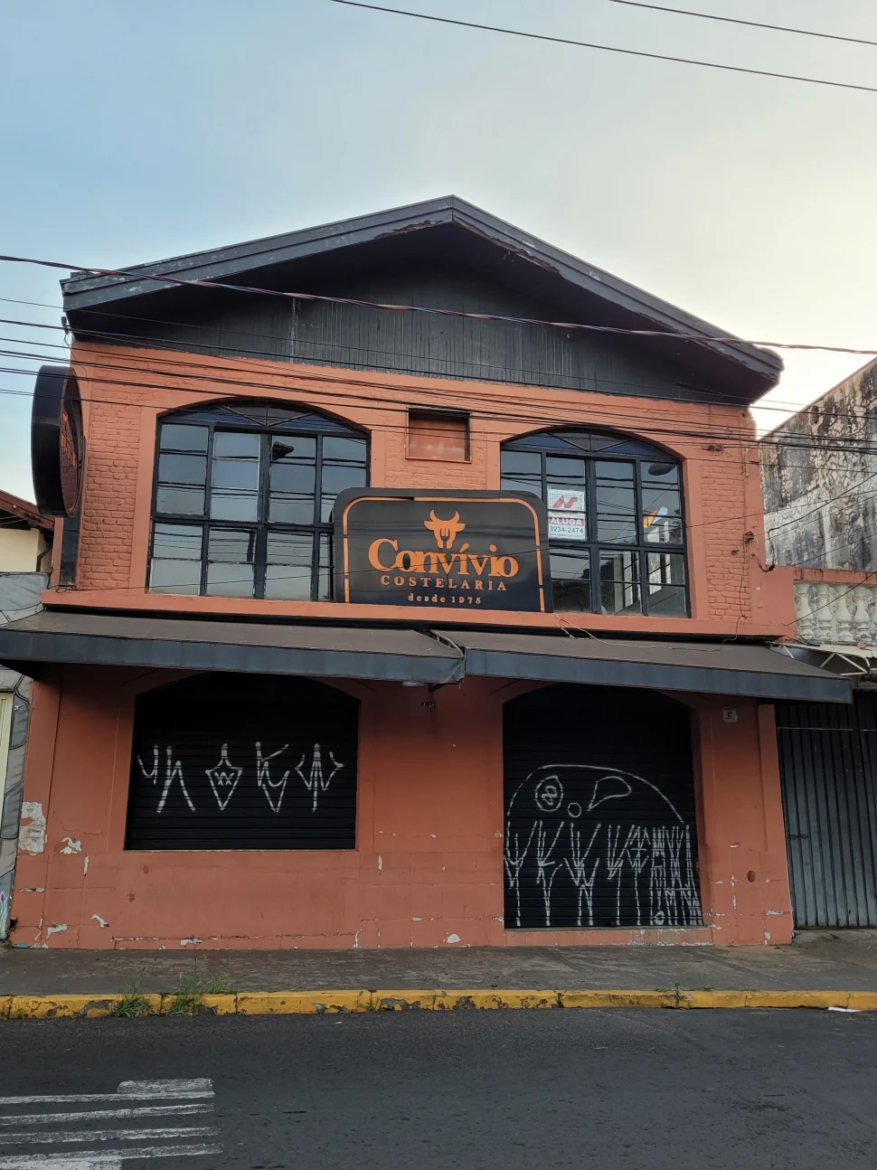 Fachada terracota do Convívio com portas fechadas, pichações e placa de aluga