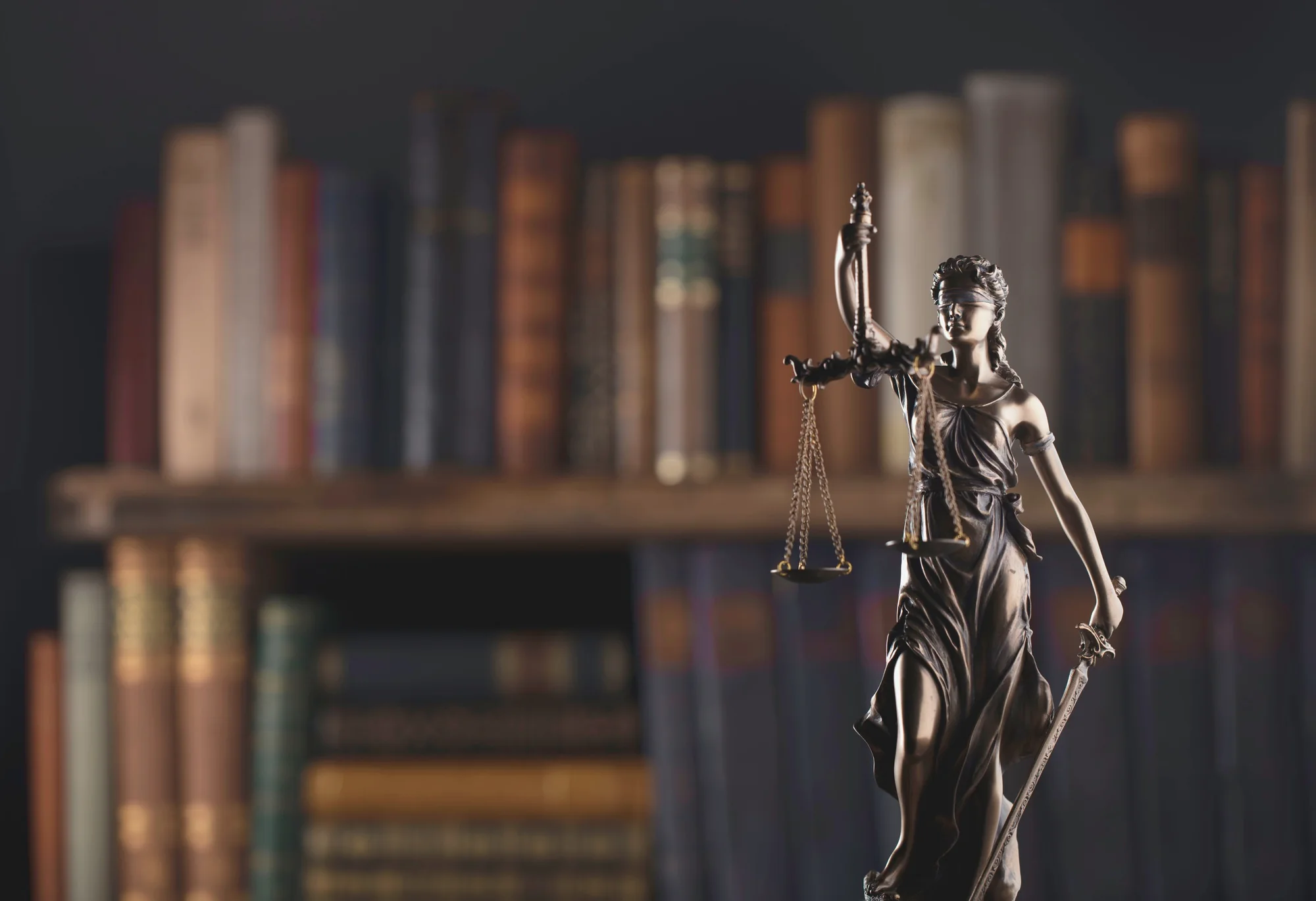 Estátua da Justiça com balança diante de uma estante de livros antigos